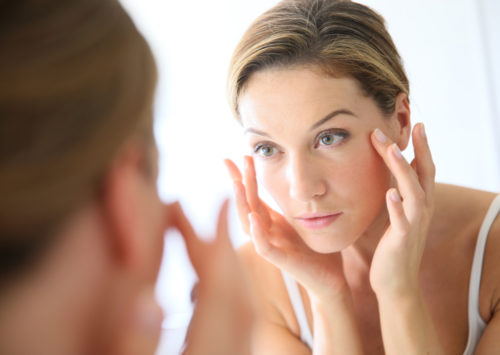 beautiful woman inspecting her skin in the mirror