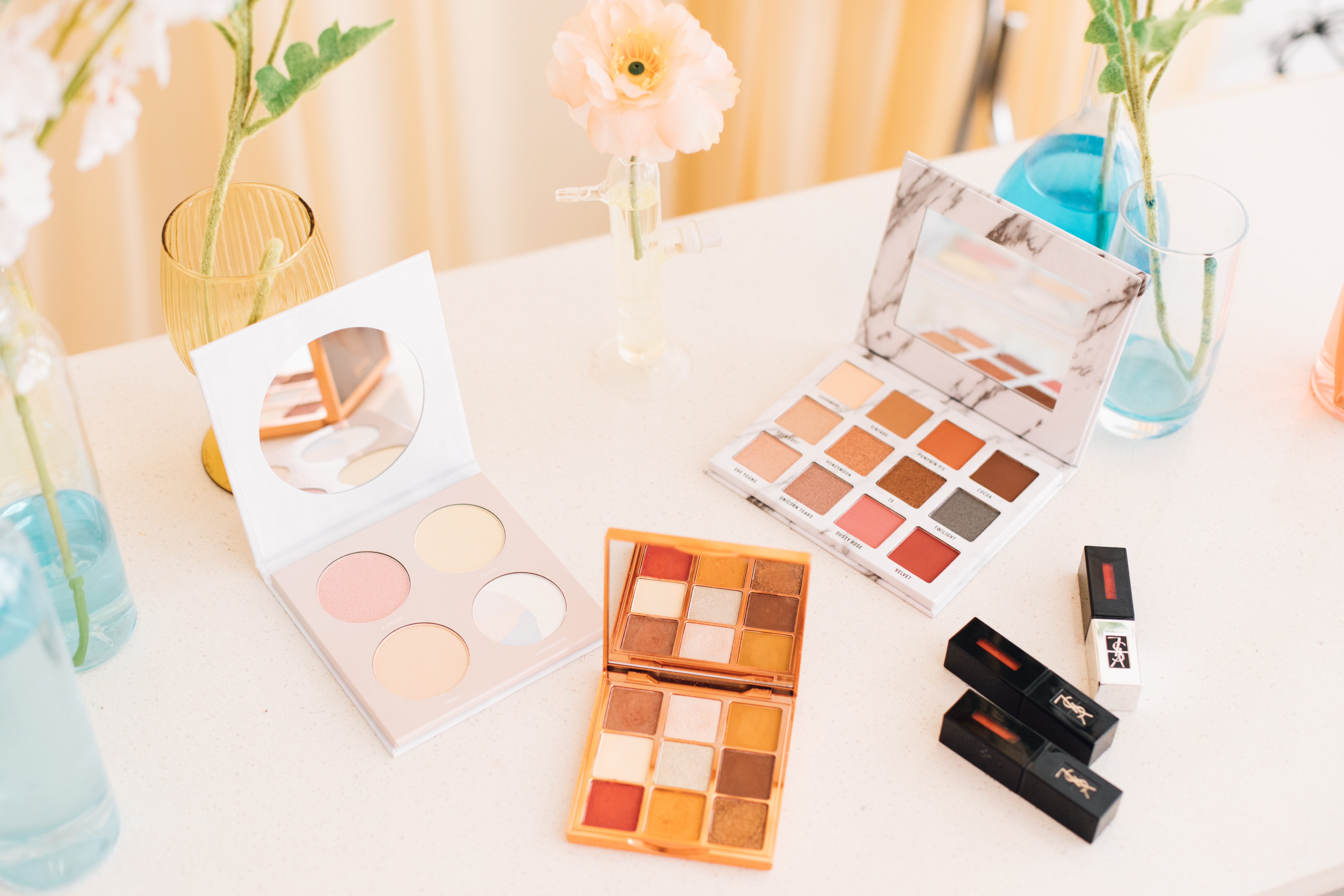 multiple makeup palettes and lipstick on a white table