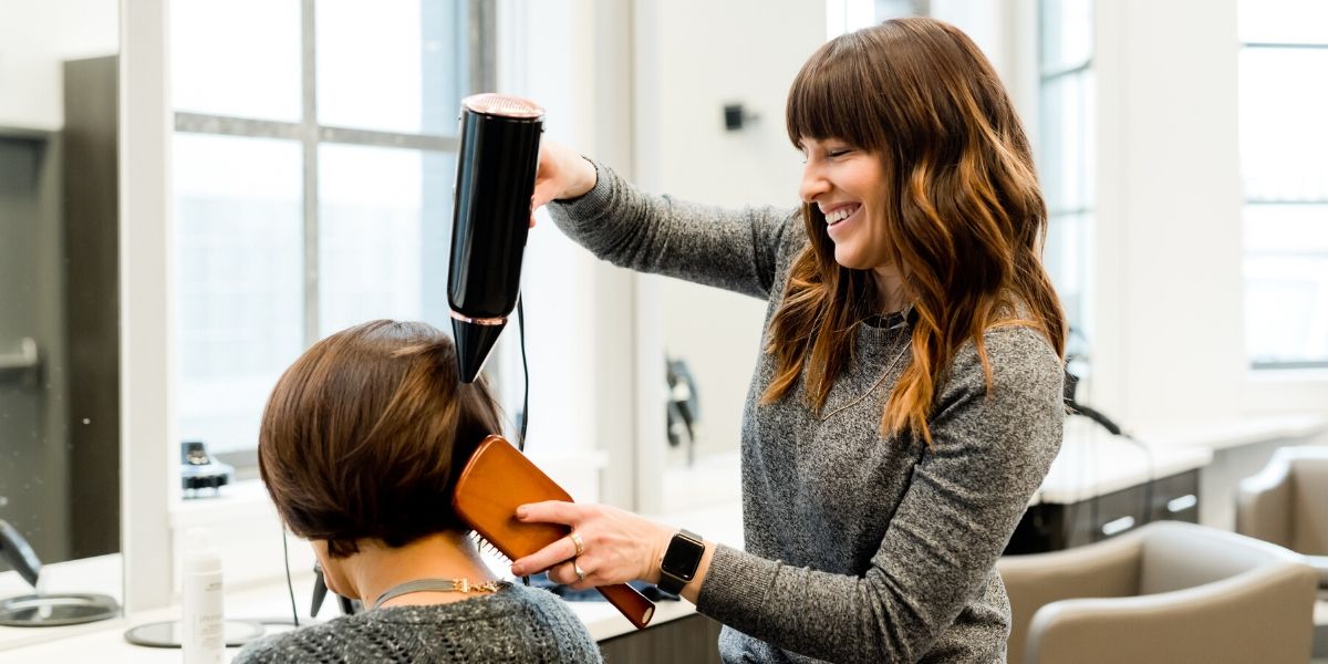 Girl blow drying a client's hair in the salon