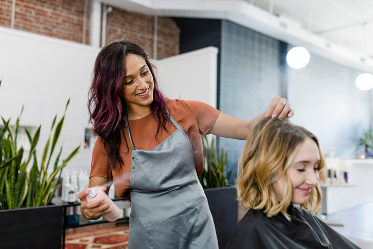 stylist spraying client’s hair